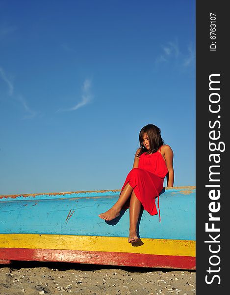 Young girl in red dress standing on boat on beach