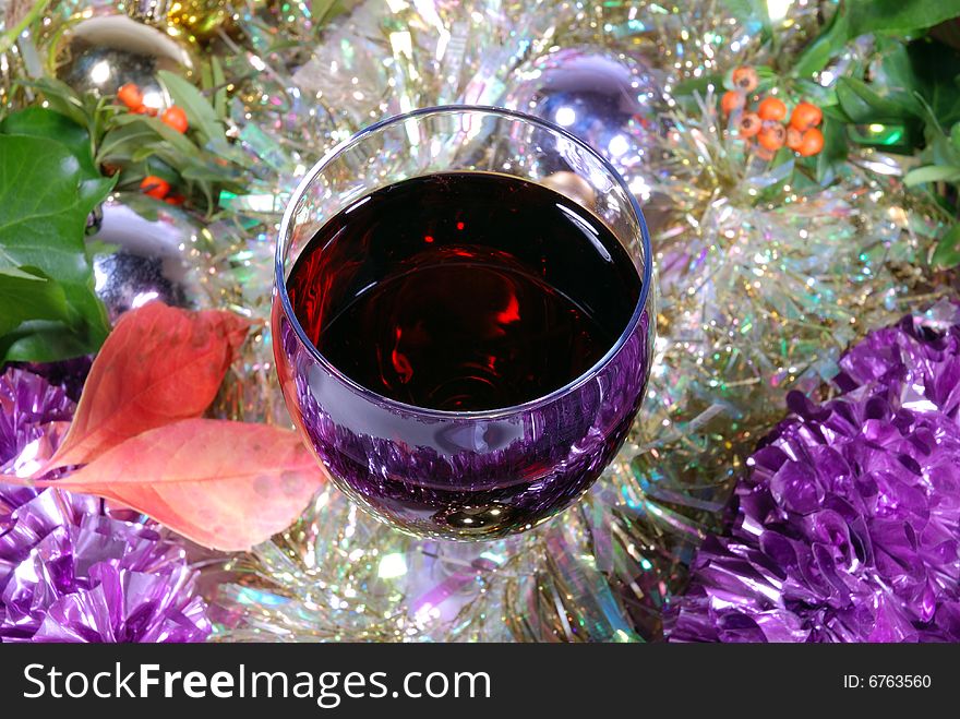 Single glass of red wine on a Christmas background with tinsel and baubles