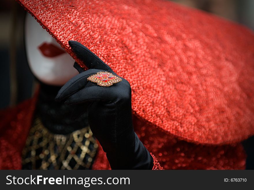 Person wearing a white mask with red hat , black gloves and ring at the Venezzia carvival. Person wearing a white mask with red hat , black gloves and ring at the Venezzia carvival