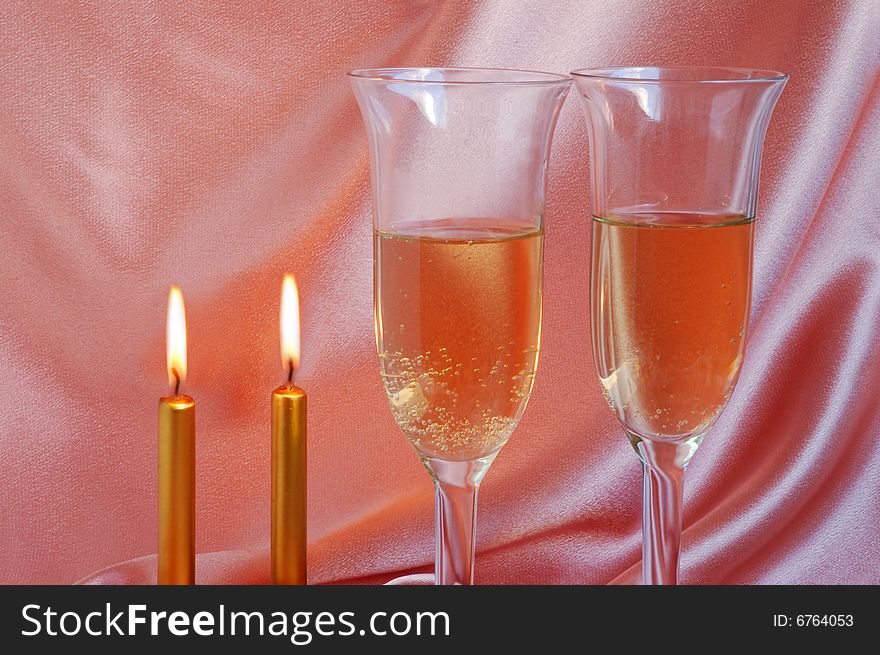 Pair of champagne flutes with candles on silk background