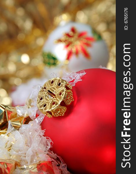 Close up with selective focus of a red Christmas ornament, along with fake snow and gold metallic background.