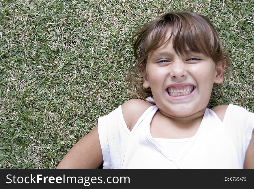 Girl laying down on grass with clenched teeth. Girl laying down on grass with clenched teeth