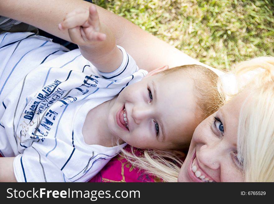 Blonder young mother posing with her baby lying on grass. Blonder young mother posing with her baby lying on grass