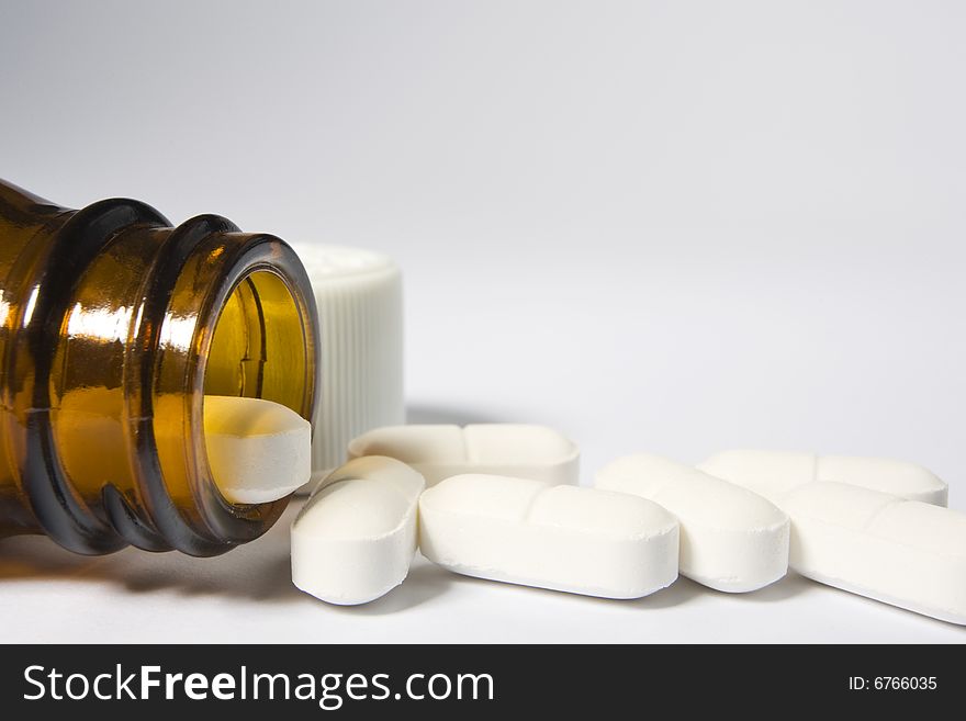 The mouth of a bottle on the left-hand side of a white background with a row of pills arranged along the bottom of the frame. The mouth of a bottle on the left-hand side of a white background with a row of pills arranged along the bottom of the frame