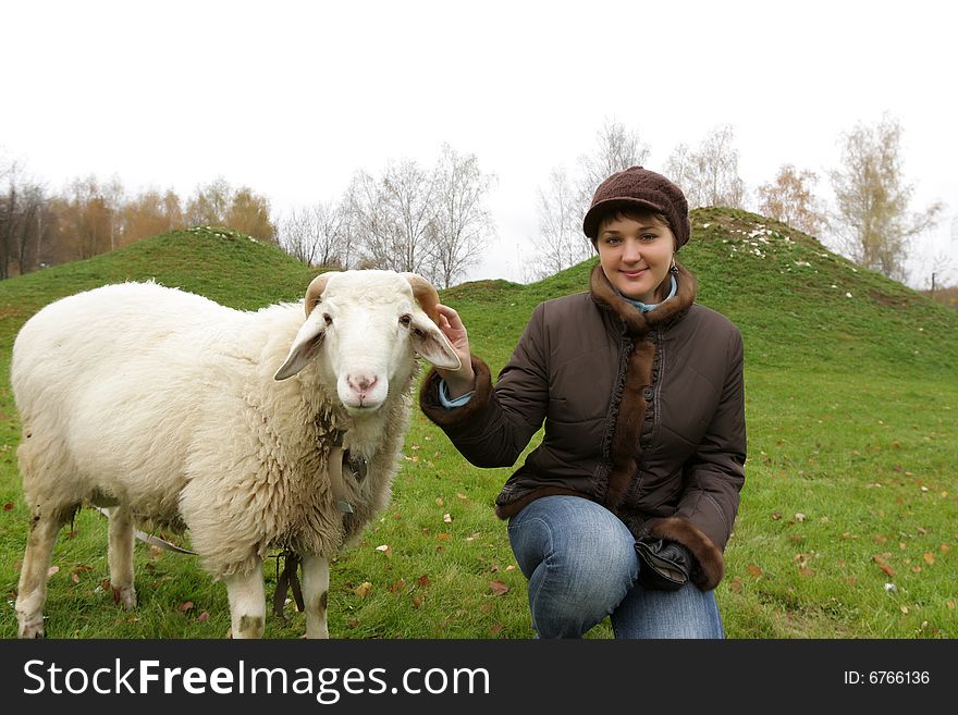 The girl poses with white sheep on lawn. The girl poses with white sheep on lawn