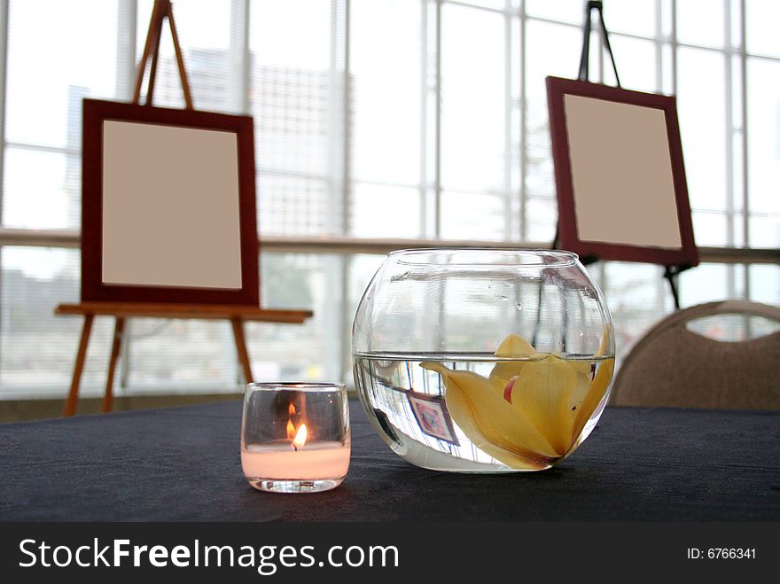 Two blank canvases sit in the background with a candle and floating flower in the foreground. Two blank canvases sit in the background with a candle and floating flower in the foreground.