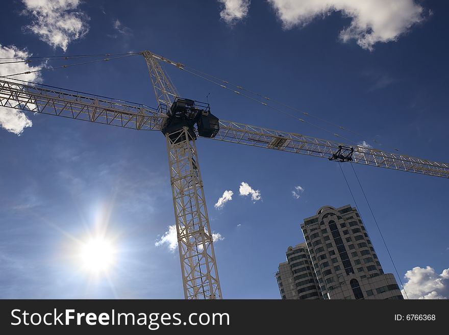 Low angle shot of a construction crane in the city against a blue sky with framed by white clouds, with a dramatic lens flare. Low angle shot of a construction crane in the city against a blue sky with framed by white clouds, with a dramatic lens flare.