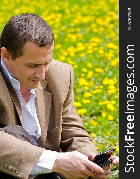 Businessman with mobile technology in a meadow with dandelions. Businessman with mobile technology in a meadow with dandelions