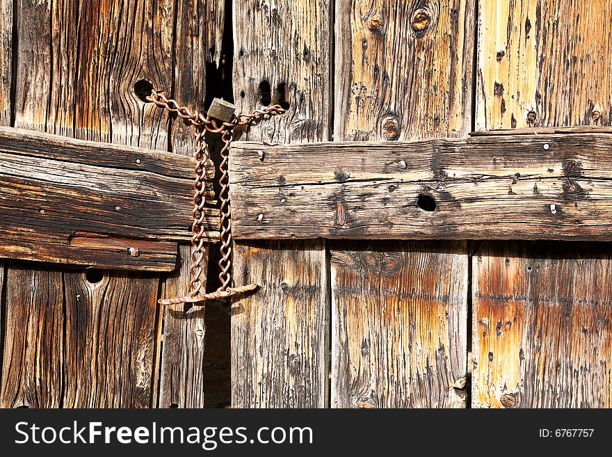 Old wooden door secured with a padlock and iron chain