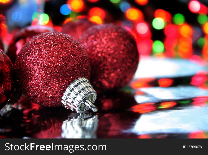 A red Christmas ornament on a reflective background with blurred lights to the far back. Copy space available. A red Christmas ornament on a reflective background with blurred lights to the far back. Copy space available.