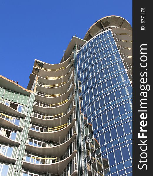 The Construction of the building. The Sun sparkles in new glass, on background blue sky.