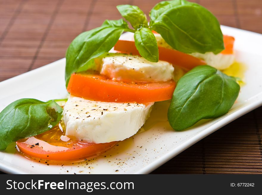 Slices of tomato and mozzarella with pepper, olive oil and mint