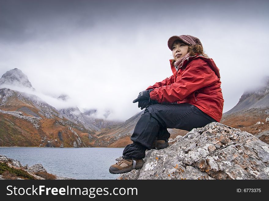 A girl is sitting on a rockï¼Œclose to the lake. A girl is sitting on a rockï¼Œclose to the lake