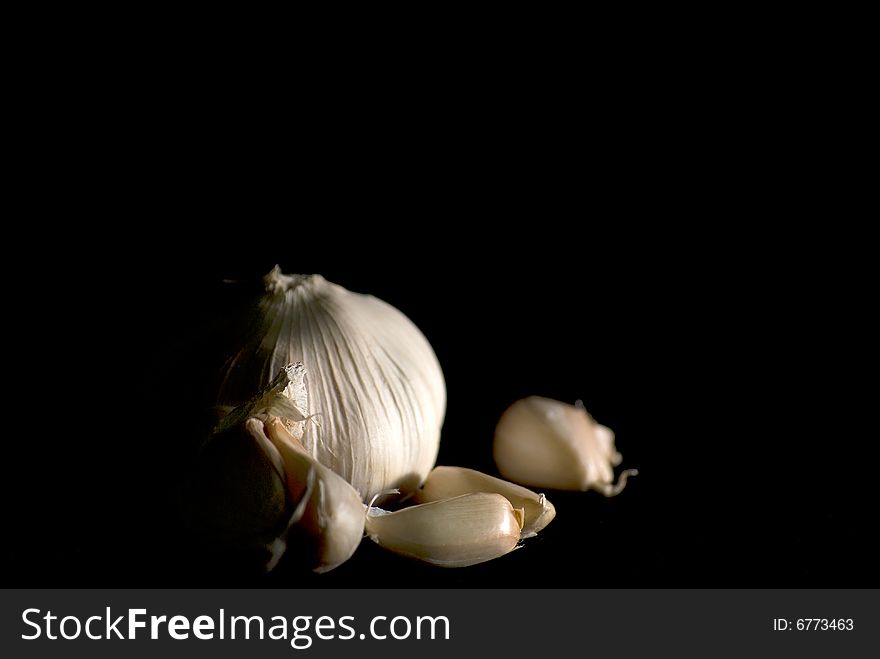 Cloves of garlic in black background.  The garlic is partially highlight and partially kept in the dark. Cloves of garlic in black background.  The garlic is partially highlight and partially kept in the dark.