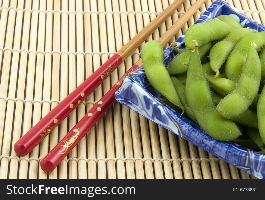 Plate of edamame with chopsticks on bamboo placemat