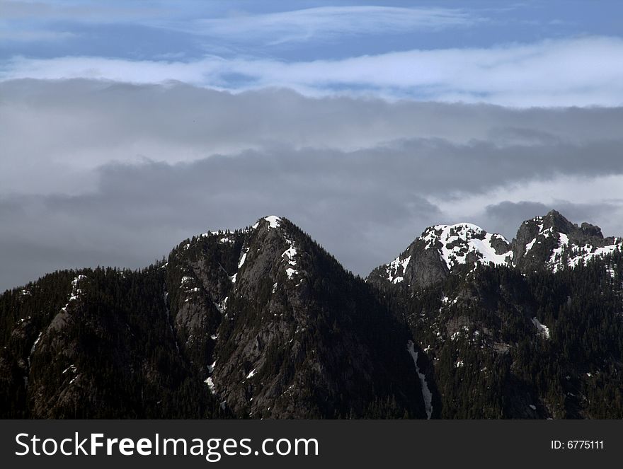 Top of a snow covered mountain range under a cloudy sky. Top of a snow covered mountain range under a cloudy sky