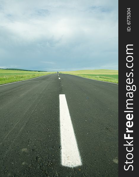 Asphalt road in field under blue sky