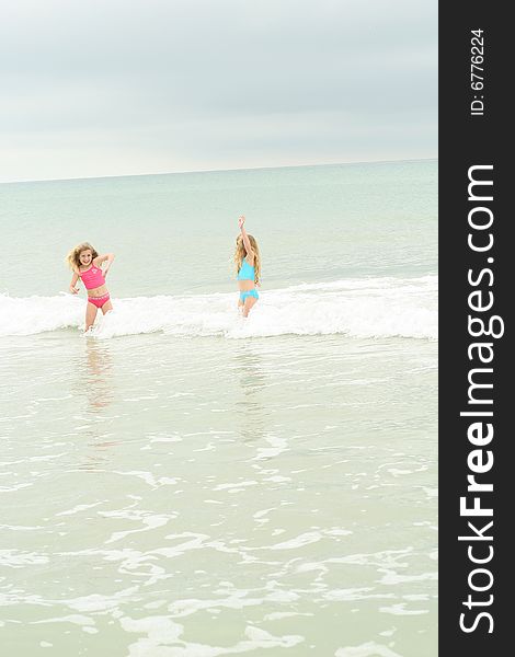 Twin sisters running from the waves vertical