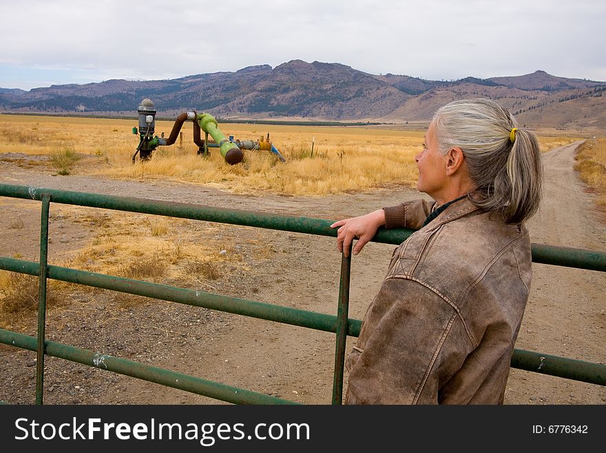 Mature female rancher standing at gate to ranch for last time.