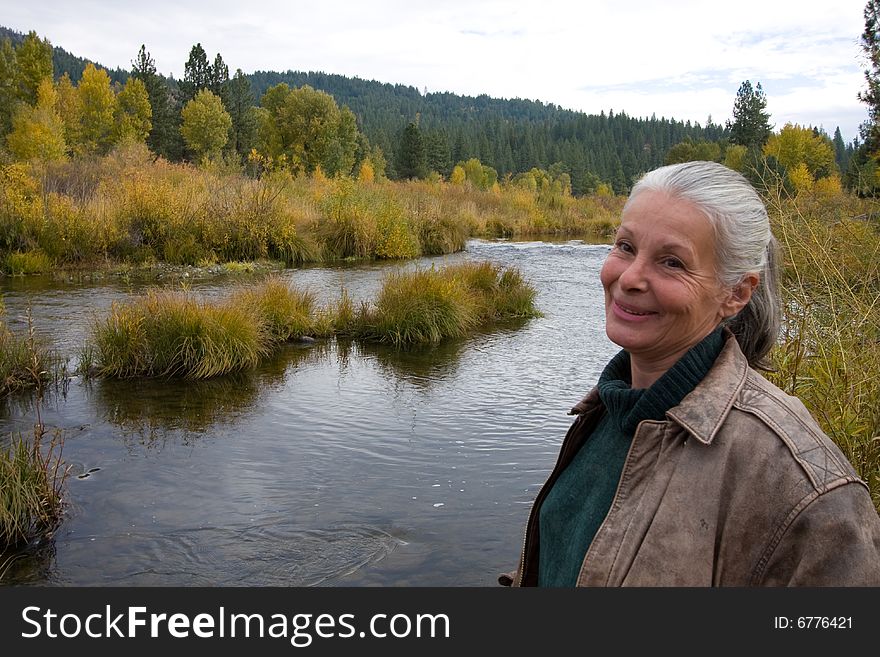 Senior woman standing on bank of river in autumn. Senior woman standing on bank of river in autumn