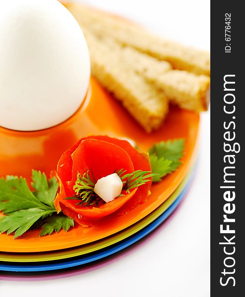 Boiled white egg in a colorful holder decorated with bread and tomato flower as decoration - closeup. Boiled white egg in a colorful holder decorated with bread and tomato flower as decoration - closeup