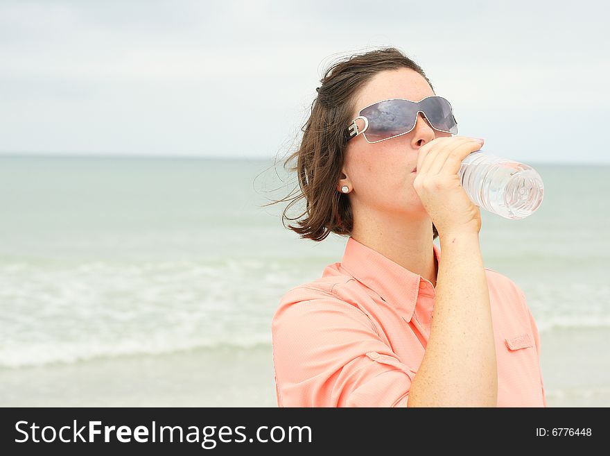 Shot of a beautiful brunette drinking water at the beach