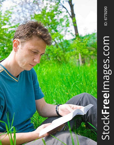 Portrait of a young man reading in grass