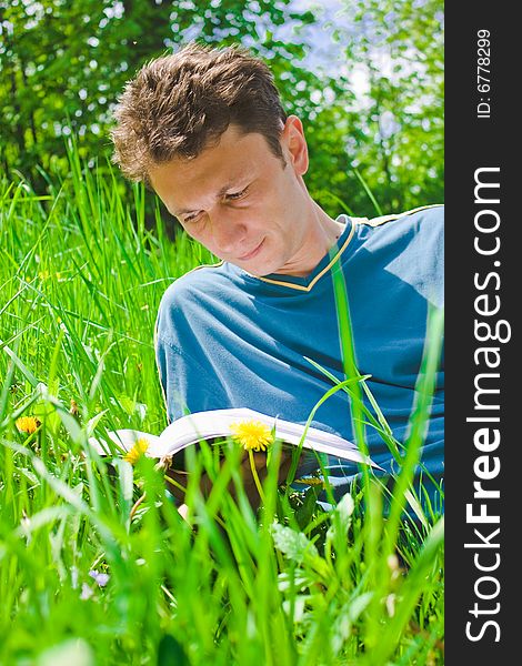 Portrait of a young man reading in grass