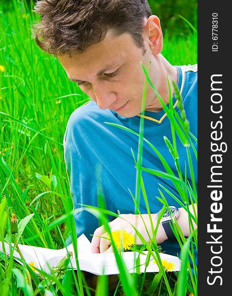 Portrait of a young man reading in grass