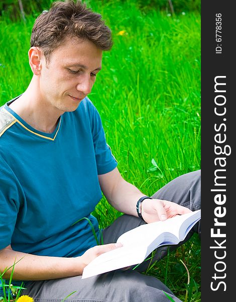 Portrait of a young man reading in grass