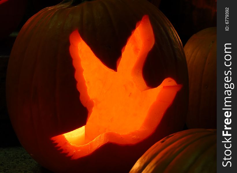 A glowing pumpkin at night, carved in the shape of a peace dove. A glowing pumpkin at night, carved in the shape of a peace dove.