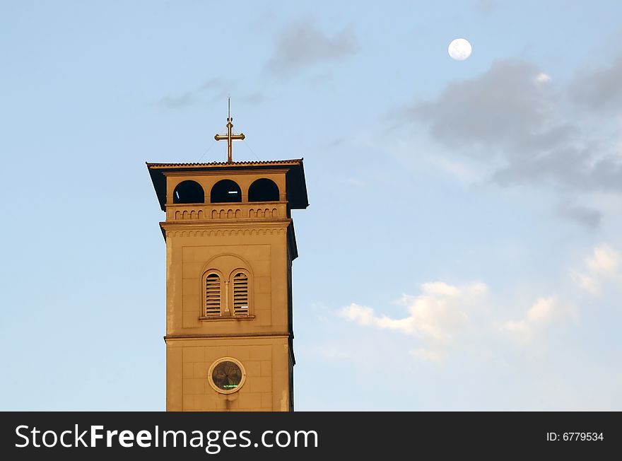 Church tower with a cross in top in a cloudy sky and Moon background.