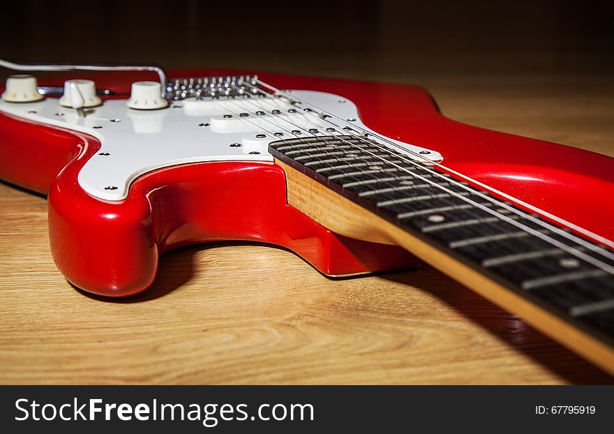 Body part of red 6 string electric guitar lying on the wooden floor closeup. Body part of red 6 string electric guitar lying on the wooden floor closeup