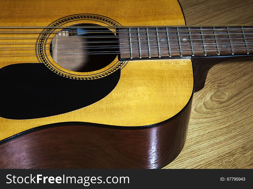 Body part of yellow 12 string guitar lying on the wooden floor closeup