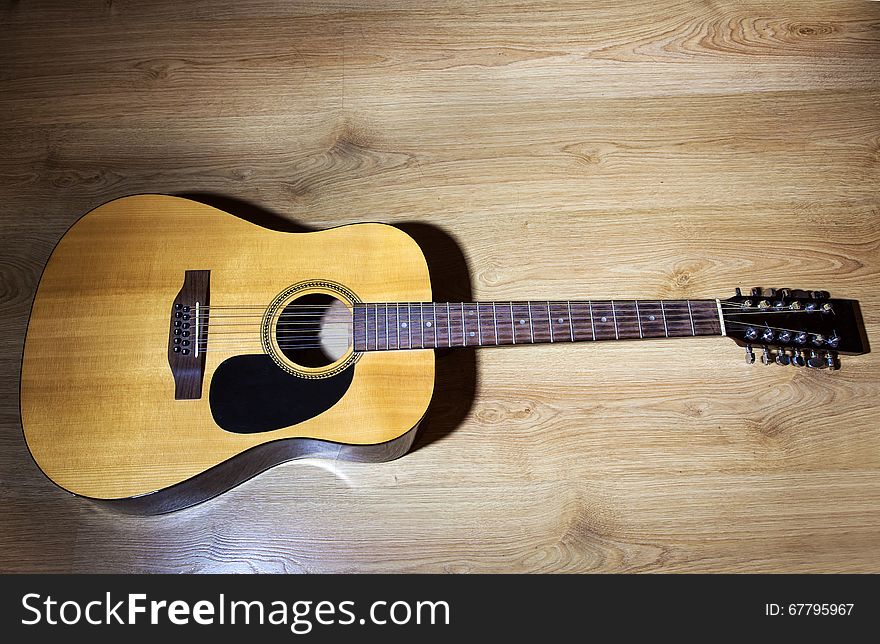 Yellow acoustic 12-strings guitar lying on wooden floor closeup