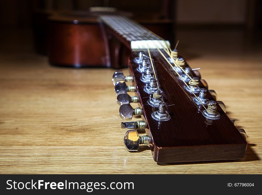 Brown head neck of 12 string guitar lyinh on wooden floor closeup. Brown head neck of 12 string guitar lyinh on wooden floor closeup