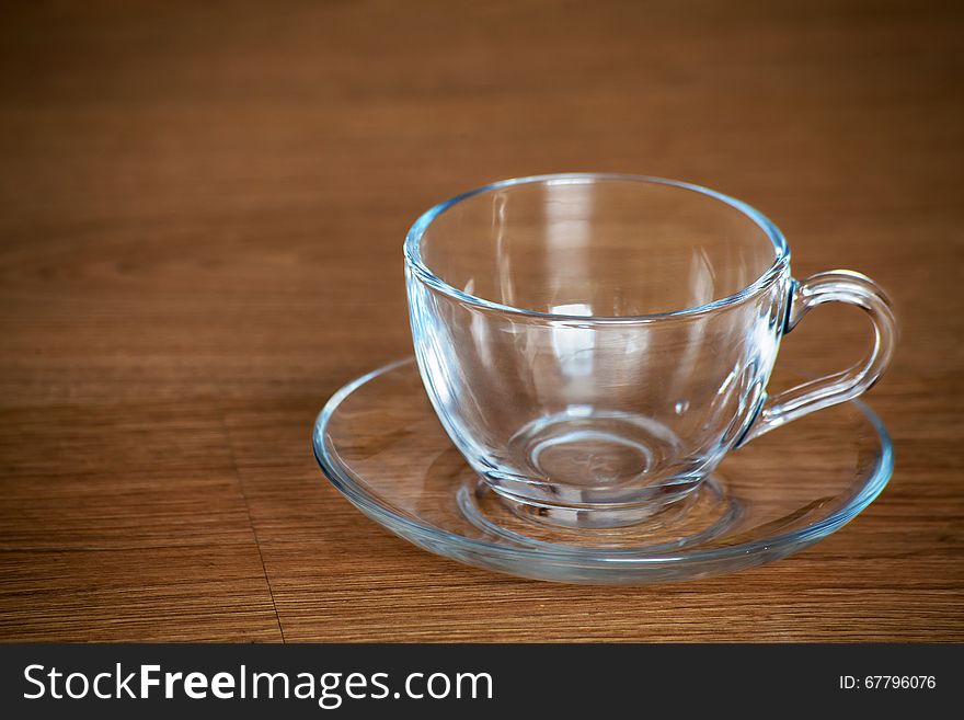 Glass cup and saucer on wooden table closeup