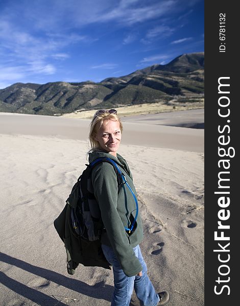 An adult woman smiling as she looks over her shoulder during a hike. Looking back the direction she has traveled in the setting sun, she shows enjoyment or happiness on her face. Great Sand Dunes National Park, Colorado. An adult woman smiling as she looks over her shoulder during a hike. Looking back the direction she has traveled in the setting sun, she shows enjoyment or happiness on her face. Great Sand Dunes National Park, Colorado