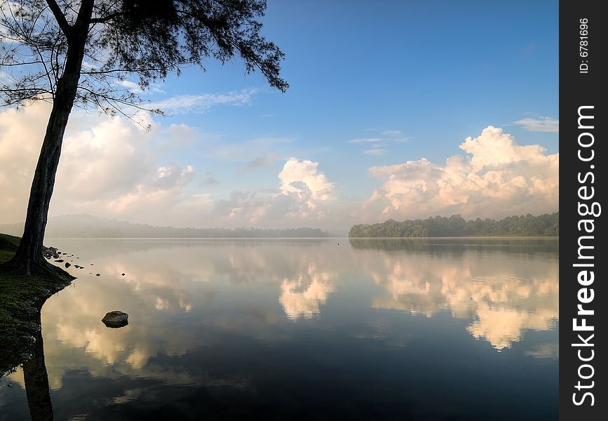 Stratocumulus clouds in a clear blue sky in the morning seen at the edge of a still lake. Stratocumulus clouds in a clear blue sky in the morning seen at the edge of a still lake