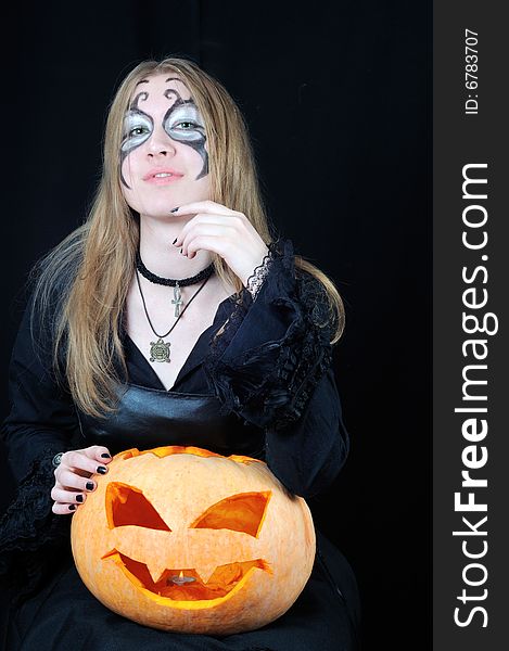 Portrait of pretty vampire girl with halloween pumpkin on black background