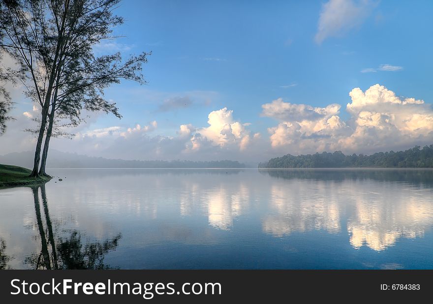 Stratocumulus clouds in a clear blue sky in the morning seen at the edge of a still lake. Stratocumulus clouds in a clear blue sky in the morning seen at the edge of a still lake