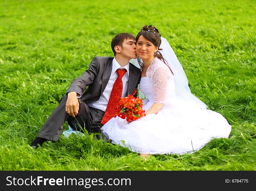 Groom and bride sitting on the green grass. Groom and bride sitting on the green grass.
