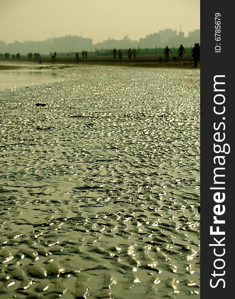 Sunlit, wet sand reliefs on the beach with a city skyline in the background