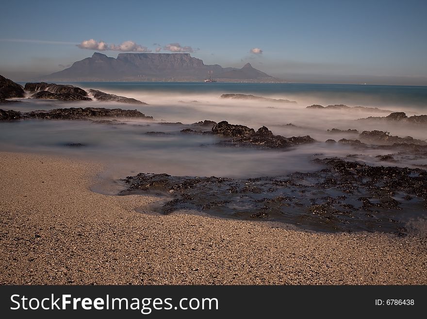 Table Mountain from Bloubergstrand with rocks in the foreground and misty water