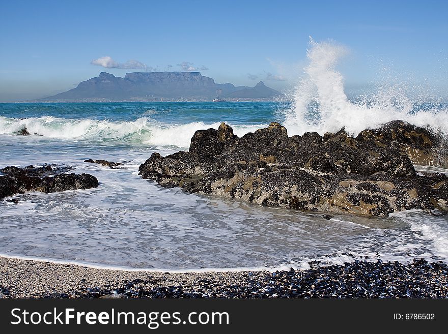 Table Mountain from Bloubergstrand with rocks in the foreground and water splash