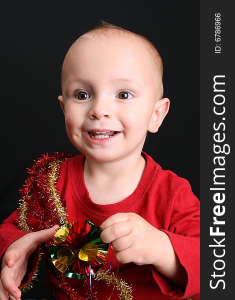 Toddler against a black background playing with christmas decorations