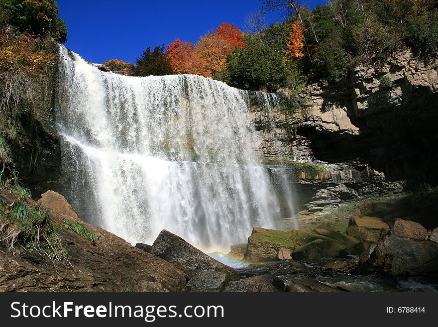 Waterfall with rainbow in the autumn forest