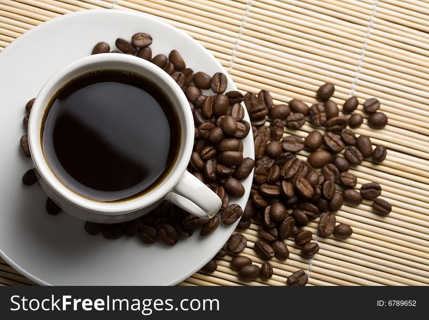 White cup of coffee and coffee beans over bamboo background