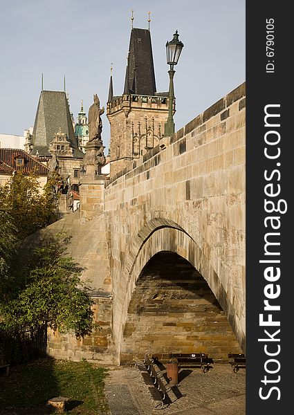 Prague to Charles bridge arch with bench for relax and bridge towers in the background.