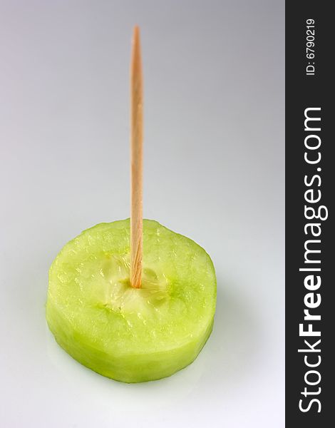 A slice of cucumber served with a toothpick on it. A slice of cucumber served with a toothpick on it